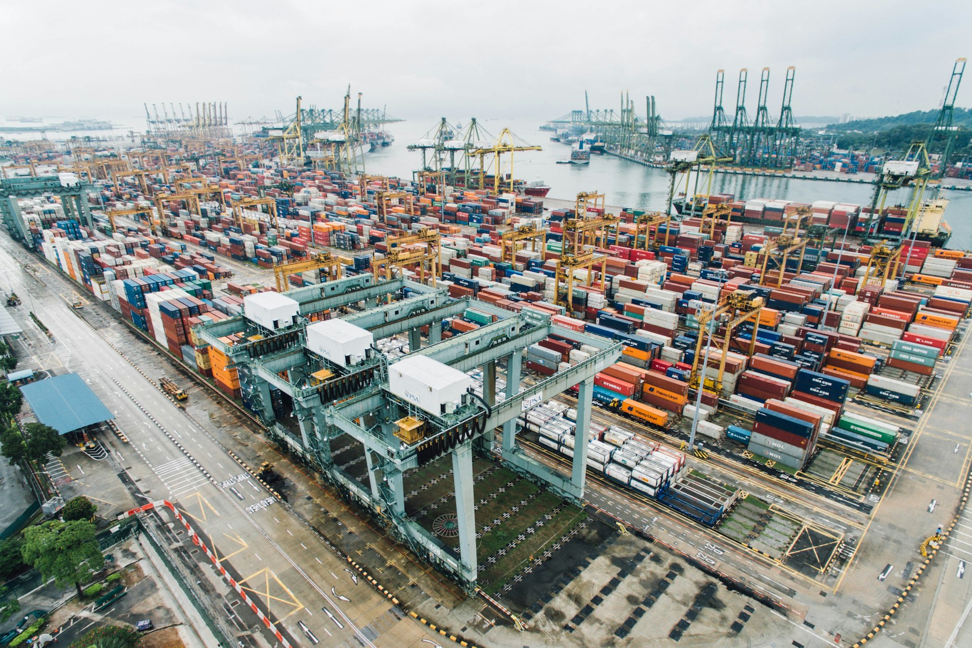 Large container ship sailing at sea with port cranes background